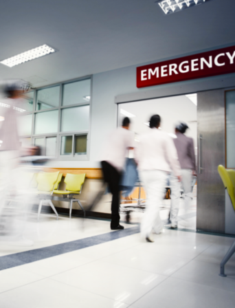 A motion blurred photograph of a patient on stretcher or gurney being pushed at speed through a hospital corridor.